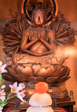 Tokyo, Japan - January 07 2020: Golden wooden statue depicting the bodhisattva Sente Kannon with thousand arms depicted sit down on a lotus in the Tendai Buddhism Gokokuin temple in the Ueno district of Tokyo with a kagamimochi rice and clementine offerinのeditorial素材