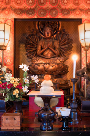 Tokyo, Japan - January 07 2020: Golden wooden statue depicting the bodhisattva Sente Kannon with thousand arms depicted sit down on a lotus in the Tendai Buddhism Gokokuin temple in the Ueno district of Tokyo with a kagamimochi rice and clementine offerinのeditorial素材