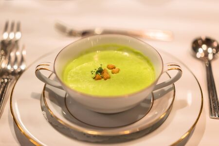 Green peas creamy soup in a white bowl decorated with gildings as appetizer of a restaurant of French cuisine.の写真素材