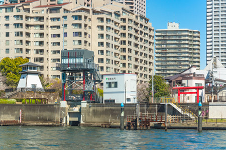 tokyo, japan - april 04 2020: Sumiyoshi Sluice gate and Ishikawajima lighthouse along the Tsukuda park of Sumida river with the red torii gate of the Sumiyoshi shrine and the buildings of Ohkawabata.のeditorial素材