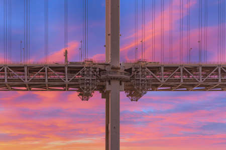 Close-up on the pillar of the Rainbow Bridge suspended in a double layer with the shuto expressway Daiba route on the upper floor and the automated yurikamome monorail line below against a sunset sky.の写真素材