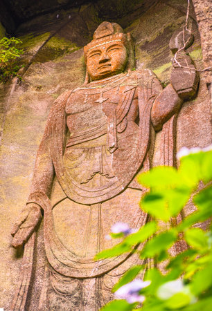 chiba, japan - july 18 2020: Low angle view on the giant relief image of Japanese hyaku-shaku kannon buddha carved in Mount Nokogiri stone quarry and a purple hydrangeas flower.のeditorial素材