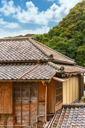 Close-up on a hip roof named yosemunezukuri ornate with decorative Onigawara tile at the end of the ridge and wooden facade named sasarako-shitami of an old traditional Japanese ryokan guesthouse.のeditorial素材
