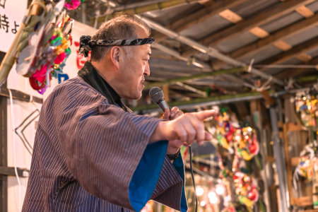 asakusa, japan - november 08 2019: Close-up on a senior man in happi kimono with an hachimaki on the head animating a lottery with a microphone during the Tori-no-Ichi Fair of Ootori shrine.のeditorial素材