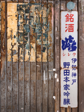 tokyo, japan - january 26 2021: Torn old vintage japanese posters of classic movie with a rusted advertising enamel sign of rice wine on the corrugated wall of Yuraku Concourse underpass in Yurakucho.のeditorial素材