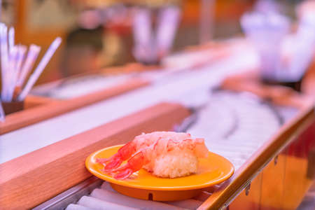 Close up on a plate carrying two pieces of fresh shrimps sushi on the roller of a conveyor belt sushi or Kaiten-zushi restaurant in Japan.の写真素材