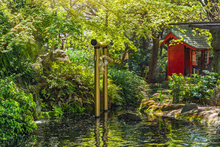 tokyo, japan - april 13 2020: Golden torii gate adorned by a shimenawa rope under the maple trees above the pond of Atago shrine with a Massha shrine dedicated to the goddess Benzaiten in background.のeditorial素材