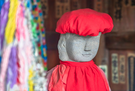 tokyo, japan - may 20 2021: Close up on the face of a Jizo statue symbol of filial piety to protect children and wearing a red knit cap with a baby bib in the Tennoji Temple of Yanaka cemetery.のeditorial素材