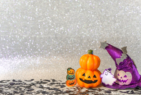 Concept photography depicting an halloween jack o lantern pumpkin head and a purple witches hat with funny ghost smiling and cardboard cutout bats against a glitter silver background of bokeh balls.の写真素材