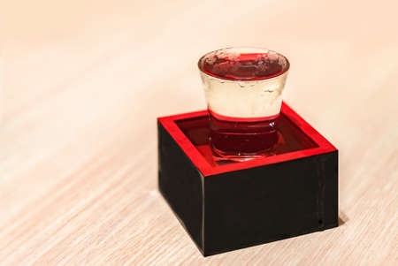 Chilled Japanese rice wine called nihonshu in a transparent overflowing sake-serving shot glass inside a traditional square lacquered wooden box called masu filled to the rim as a sign of prosperity.の写真素材