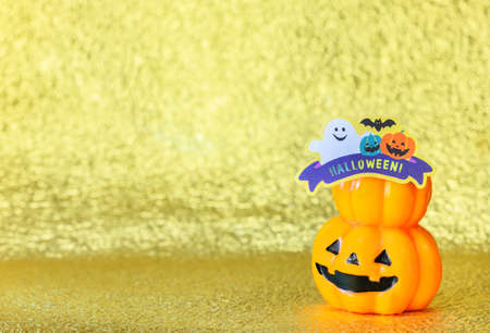 Studio photography depicting a smiling halloween jack o lantern pumpkin head with cardboard cutout of a funny ghost and bats with the word Halloween! against a glitter golden background.の写真素材
