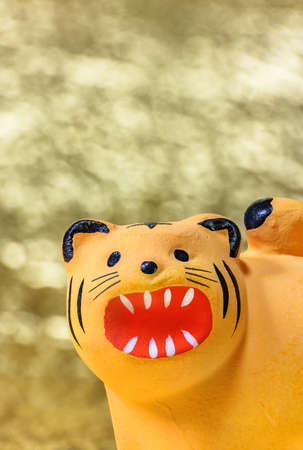 Japanese New Year's Greeting Card depicting a close up on the cute face of a Zodiac animal handmade figurine of the tiger for 2022 roaring against a glittering gold background.の写真素材