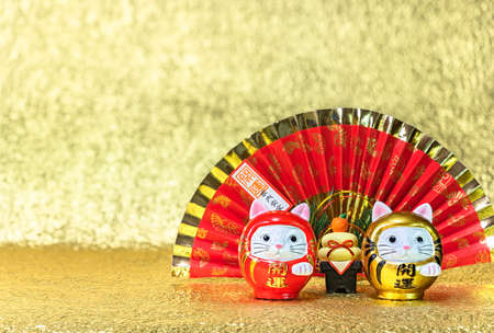 Japanese New Year's Greeting Card depicting a red handheld fan written good luck for a safe house with two cat daruma figurines written good luck against a golden background.の写真素材