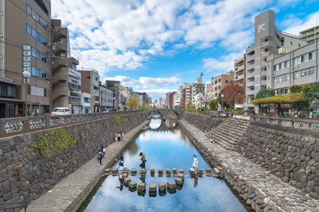 nagasaki, kyushu - december 12 2021: Group of young tourists girls walking on a stone path crossing the Nakashima river in front of Meganebashi or Spectacles Bridge looking for heart shaped stones.のeditorial素材