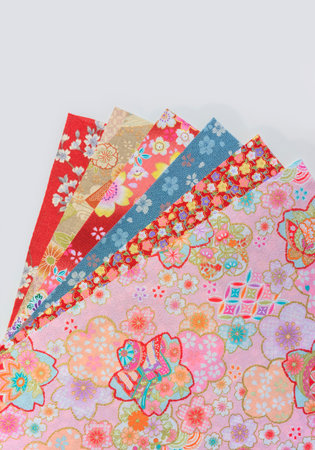 Photograph of a stack of spread-out traditional Japanese furoshiki fabrics decorated with a range of floral patterns designs such as cherry, plum, cosmos or peony blossoms on a white background.の写真素材