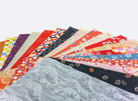 An arrangement of Japanese traditional patterns, from the Seigaiha waves, the Shippo Tsunagi circles and Asanoha leaves, adorn a spread-out stack of furoshiki fabrics on a white background.の写真素材