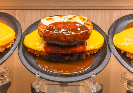 Japanese food model or shokuhin sample depicting a fake omurice omelette made with fried rice and topped by a hamburg steak with melted gruyere cheese and a brown sauce, the favorite dish of children.の写真素材