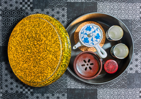Overhead view of a japanese tea set with ceramic ware Chawan Cups, a tea-pot and a chakoboshi container for collecting excess tea, stored in a golden lacquer box on a fabric with traditional patterns.の写真素材