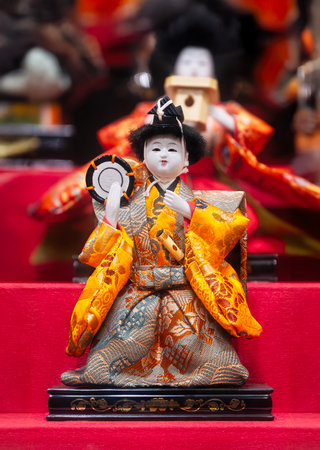 Focus on a single Japanese Hina doll dressed in ornate kimono playing a tsuzumi drum displayed on a red tiered platform for Hinamatsuri, a traditional festival celebrating girls' health and happiness.の写真素材