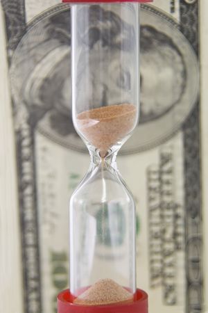 Closeup view of sand flowing through an hourglass on the background money
