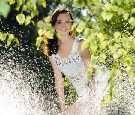 cute brunette in white dress standing behind water splash の写真素材