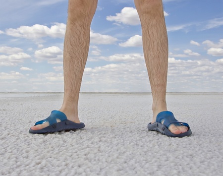 tanned legs of man wearing flip flops standing on the beachの写真素材