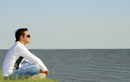 young caucasian man sitting alone and looking to the seaの写真素材