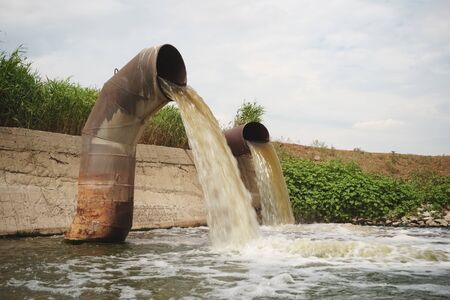 Wastewater from two large rusty pipes merge into the river in clouds of steamの写真素材