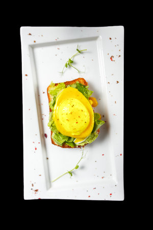 Delicious poached egg sandwich on white plate isolated on black background