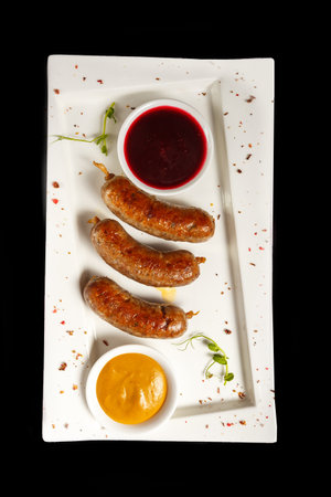 Grilled sausages with sauce on a white plate on a black backgroundの写真素材