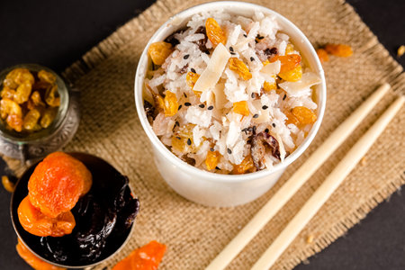 Rice with raisins and dried apricots in a bowl on a black background