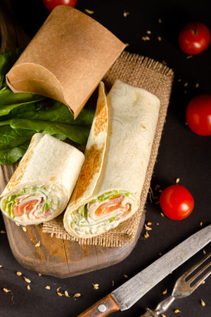 tortilla wrap with salmon, cheese and vegetables on black background