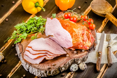 smoked ham on wooden cutting board with vegetables and cutleryの写真素材