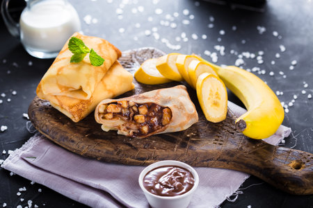 Pancakes with banana, nuts and chocolate sauce on wooden boardの写真素材