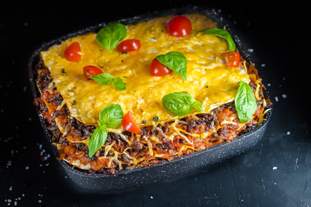 Lasagna with meat, cheese and vegetables on a black background.の写真素材