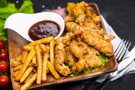 Fried chicken wings with French fries and sauce on a wooden plateの写真素材