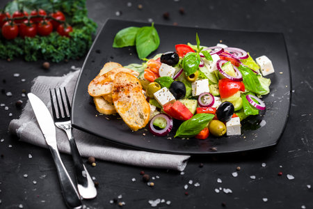 Greek salad with grilled chicken, feta cheese and fresh vegetables on black backgroundの写真素材