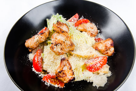 Caesar salad with grilled chicken on a black plate on a white backgroundの写真素材