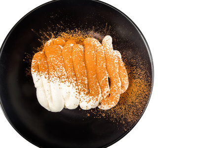 Cake with cream and cocoa powder on black plate isolated on white background