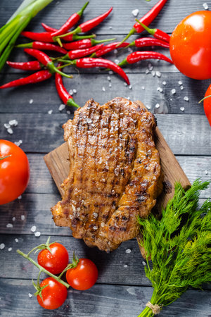 Grilled beef steak on cutting board with vegetables on wooden background.の写真素材