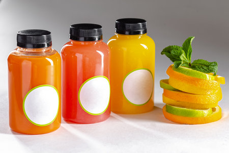 Orange and lemon juices in bottles with mint leaves on a white backgroundの写真素材
