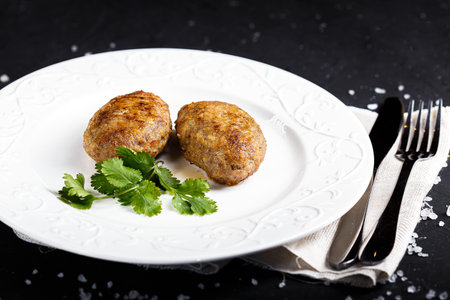 Fried meatballs with parsley on a white plate on a black background