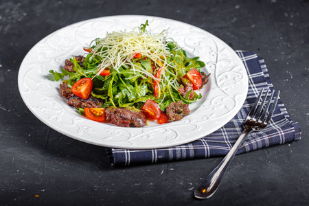 Salad with beef, arugula and tomato on a black backgroundの写真素材