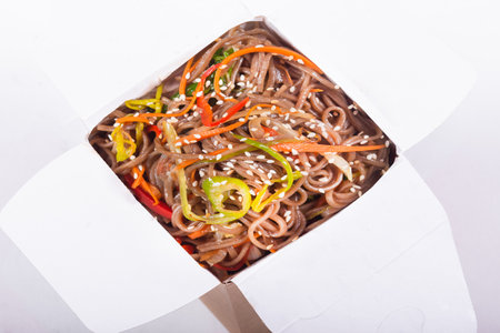 Soba noodles with vegetables in a paper box on a white background