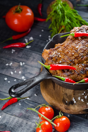 Grilled beef steak with red hot chili pepper and tomato on wooden backgroundの写真素材