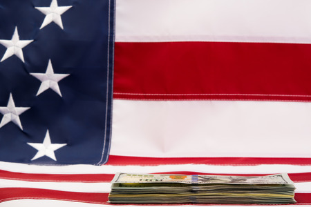 a stack of bills lying on a background of the American flagの写真素材