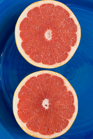 two ripe grapefruit cut and lie on a blue backgroundの写真素材