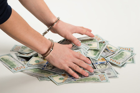 hands handcuffed over a bunch of dollars, over white backgroundの写真素材