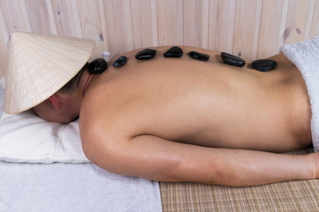 man on massage table gets relax from black stonesの写真素材