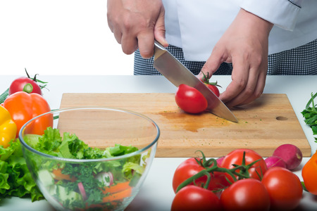 cook cuts a tomato for salad on a background of vegetablesの写真素材